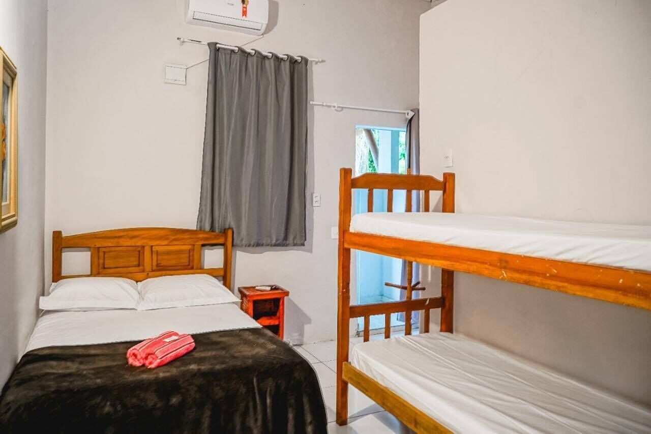 A room with a wooden bed, a bunk bed, a small table, and a window with curtains.