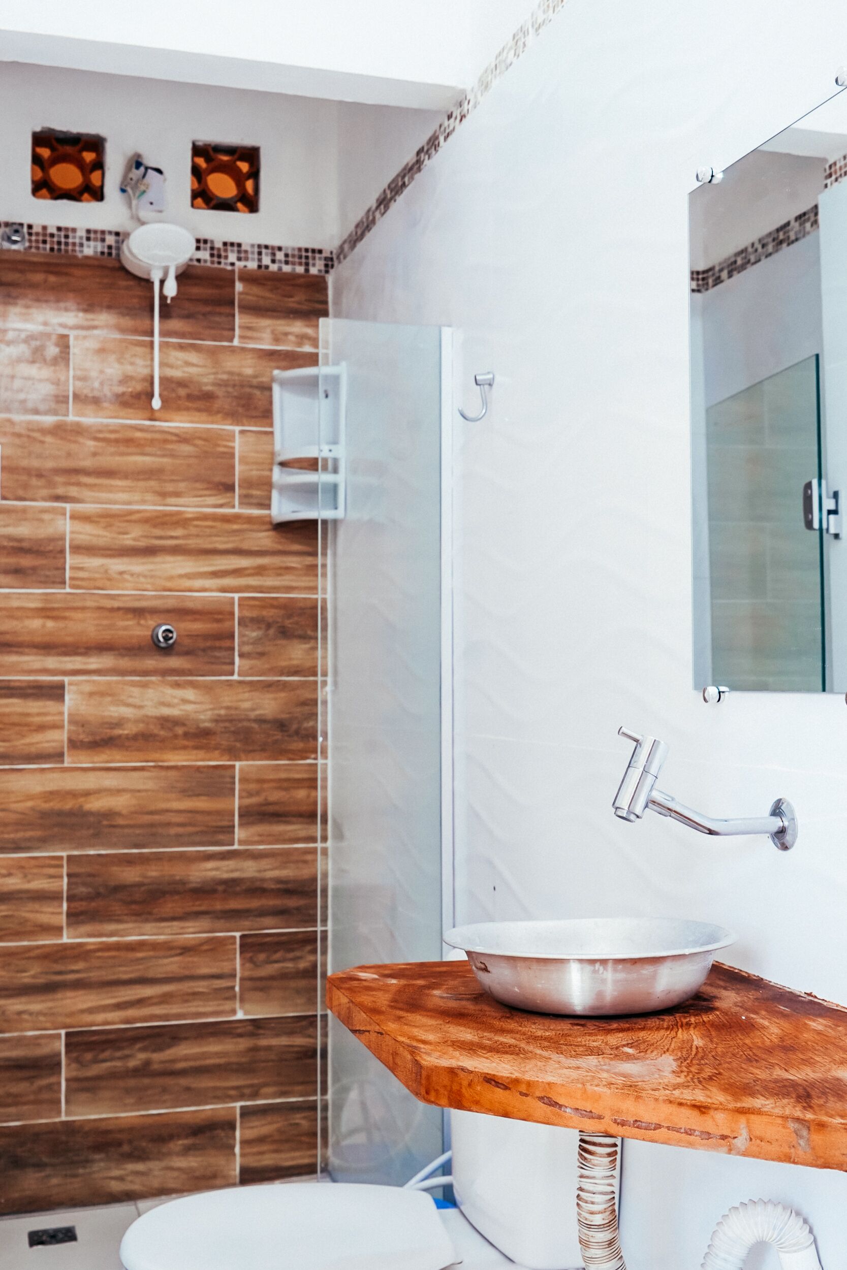 Une salle de bain avec un mur en bois, un lavabo blanc avec un receveur, et une douche en verre.