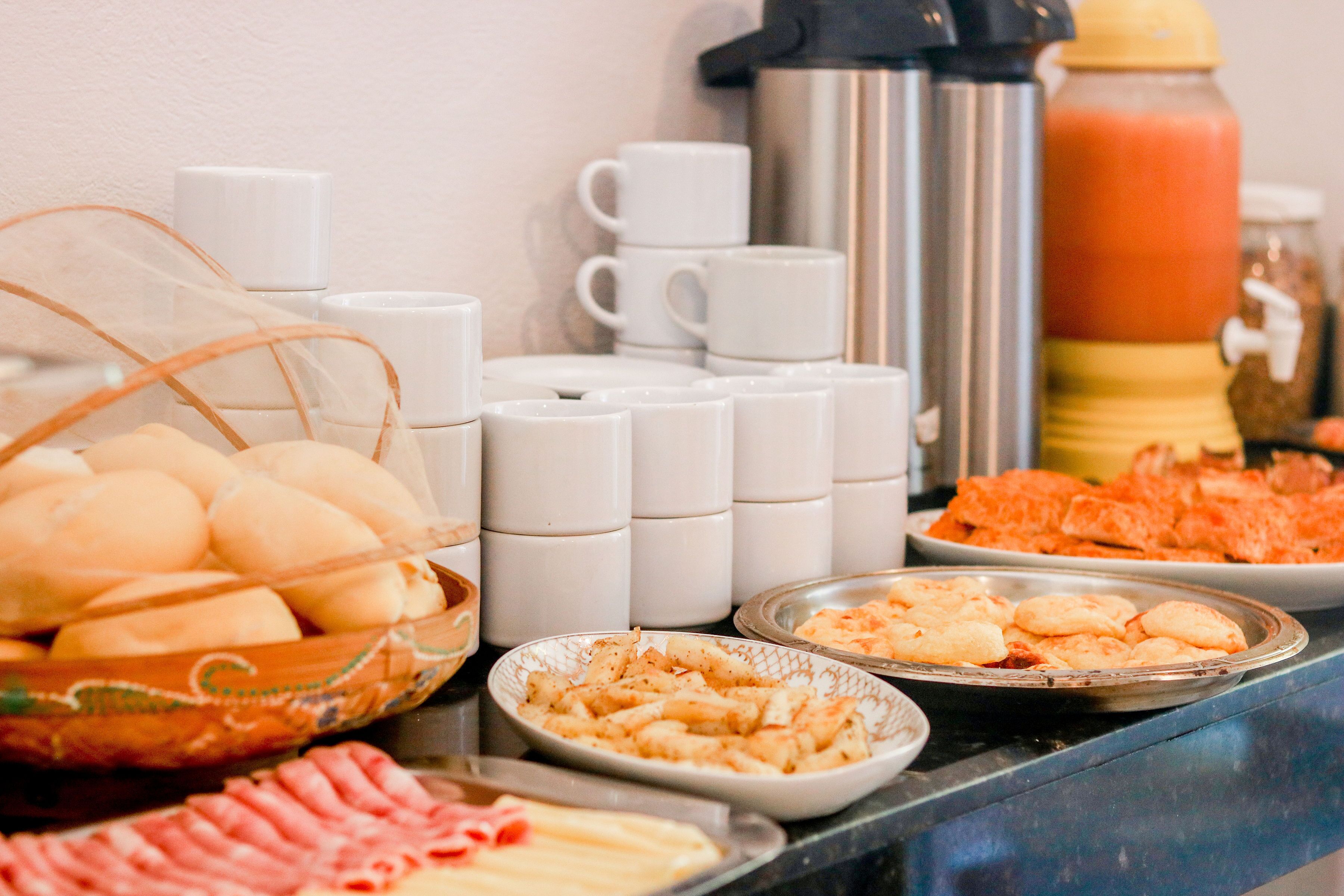 A buffet table with various food items, including bread, pastries, and a hot beverage dispenser.