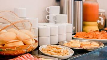 Una mesa de buffet con diversos alimentos, como pan, pasteles y un dispensador de bebidas calientes.