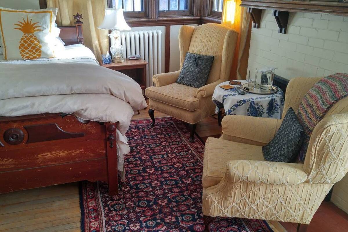 A cozy room with a wooden bed, two armchairs, a small table with a lamp, and a patterned rug.