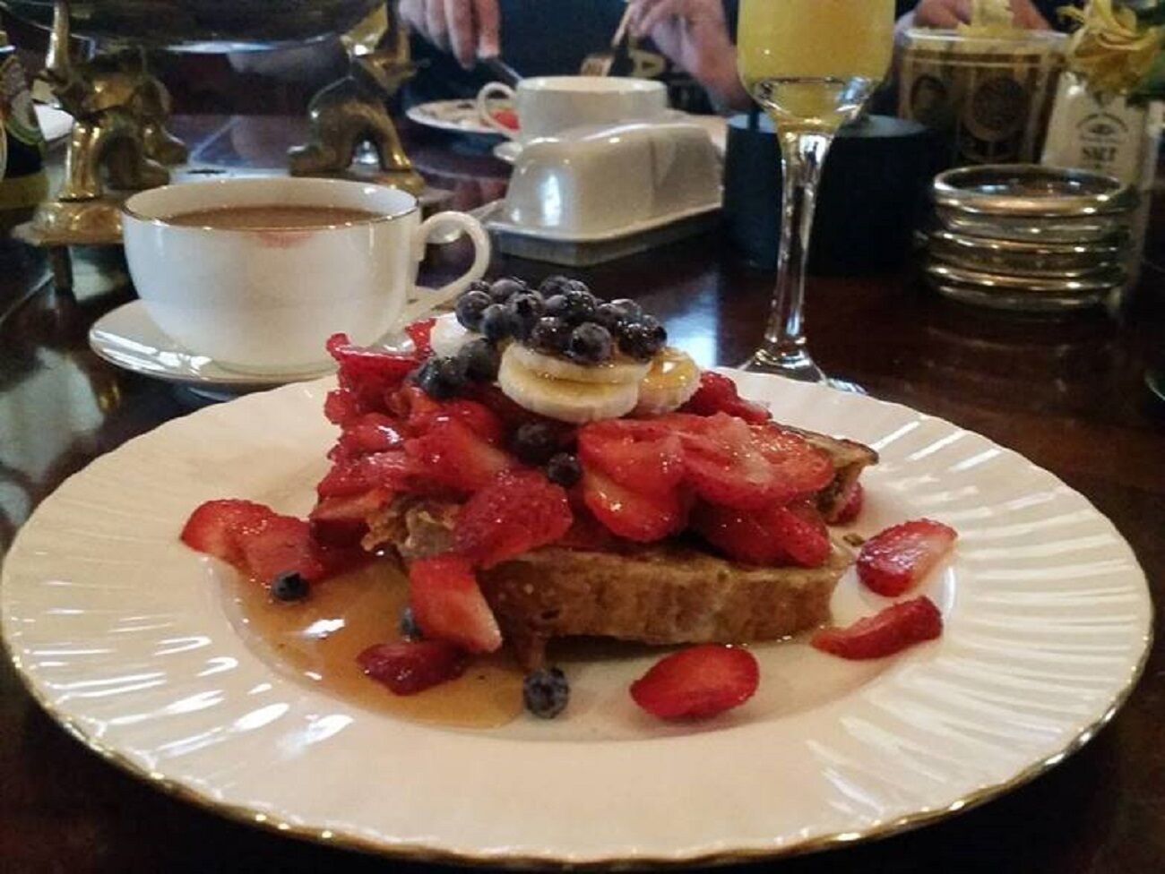 A dessert plate with a slice of toast topped with strawberries, blueberries, and a dollop of cream, accompanied by a cup of coffee and a glass of orange juice.