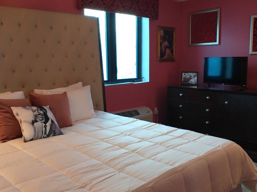 Un dormitorio con una cama grande, un aparador, un televisor y una ventana con cortinas.