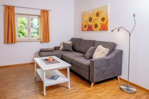 A living room with a grey sofa, a white coffee table, a floor lamp, and a painting of sunflowers.