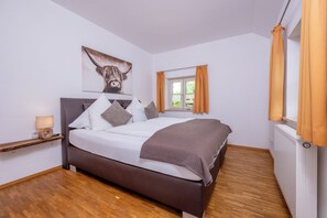 A bedroom with a bed, a headboard with a mounted artwork, a bedside table with a lamp, and a window with curtains.