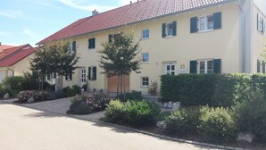 A two-story building with a red-tiled roof, numbered 20, and a paved driveway with landscaped gardens.