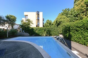 A swimming pool with a modern design, surrounded by well-maintained hedges and a building in the background. - Appartamento Faelmo Luxury (Sirmione)