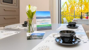 Une table avec des brochures, un vase rempli de fleurs blanches et, par la fenêtre, une vue sur le feuillage jaune.