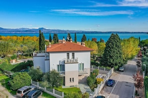 A modern two-story building with a red-tiled roof, surrounded by greenery and a view of a lake and mountains. - Appartamento Faelmo Luxury (Sirmione)