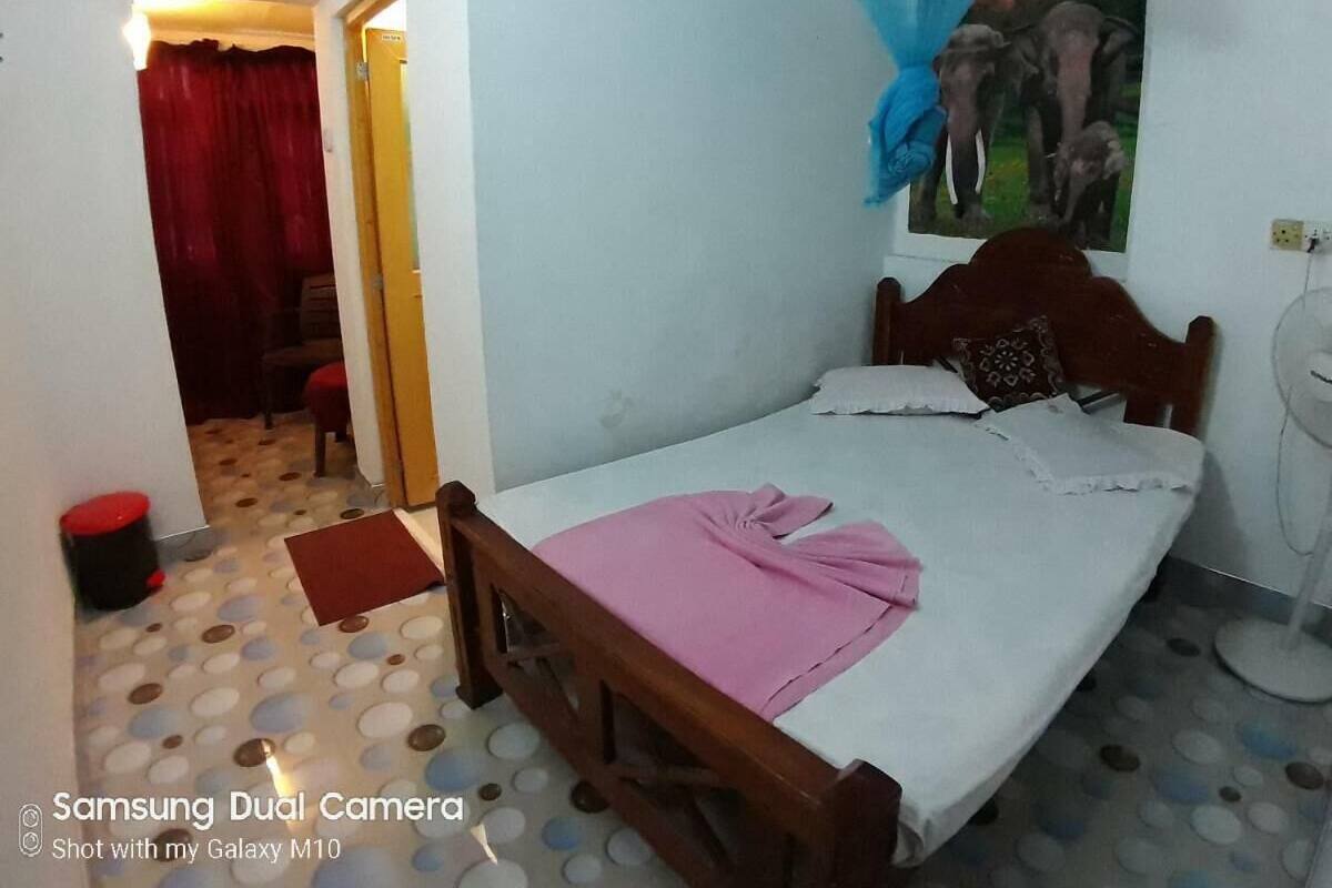 A bedroom with a bed, a wooden headboard, a red curtain, a painting of elephants, and a fan.