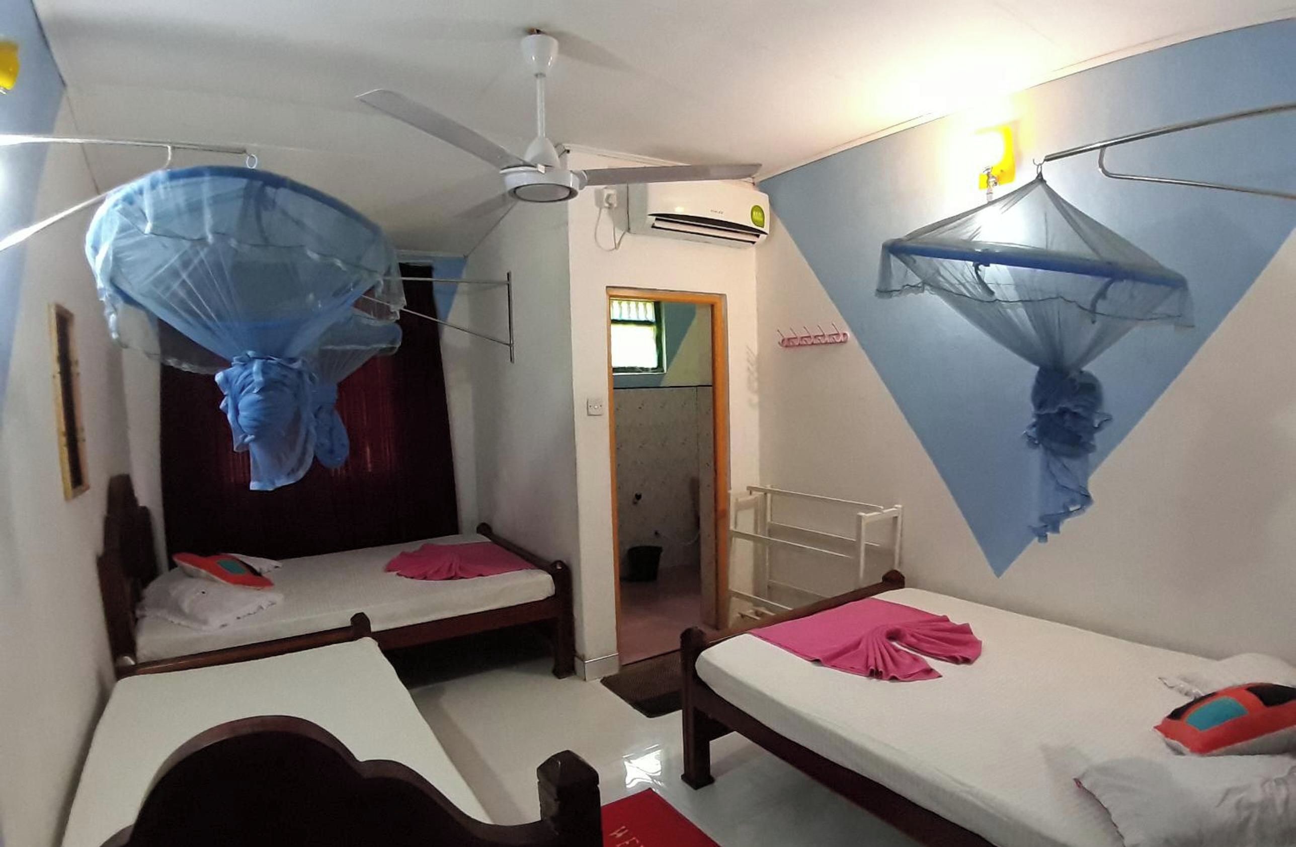 A room with two beds, a ceiling fan, an air conditioning unit, and mosquito netting.