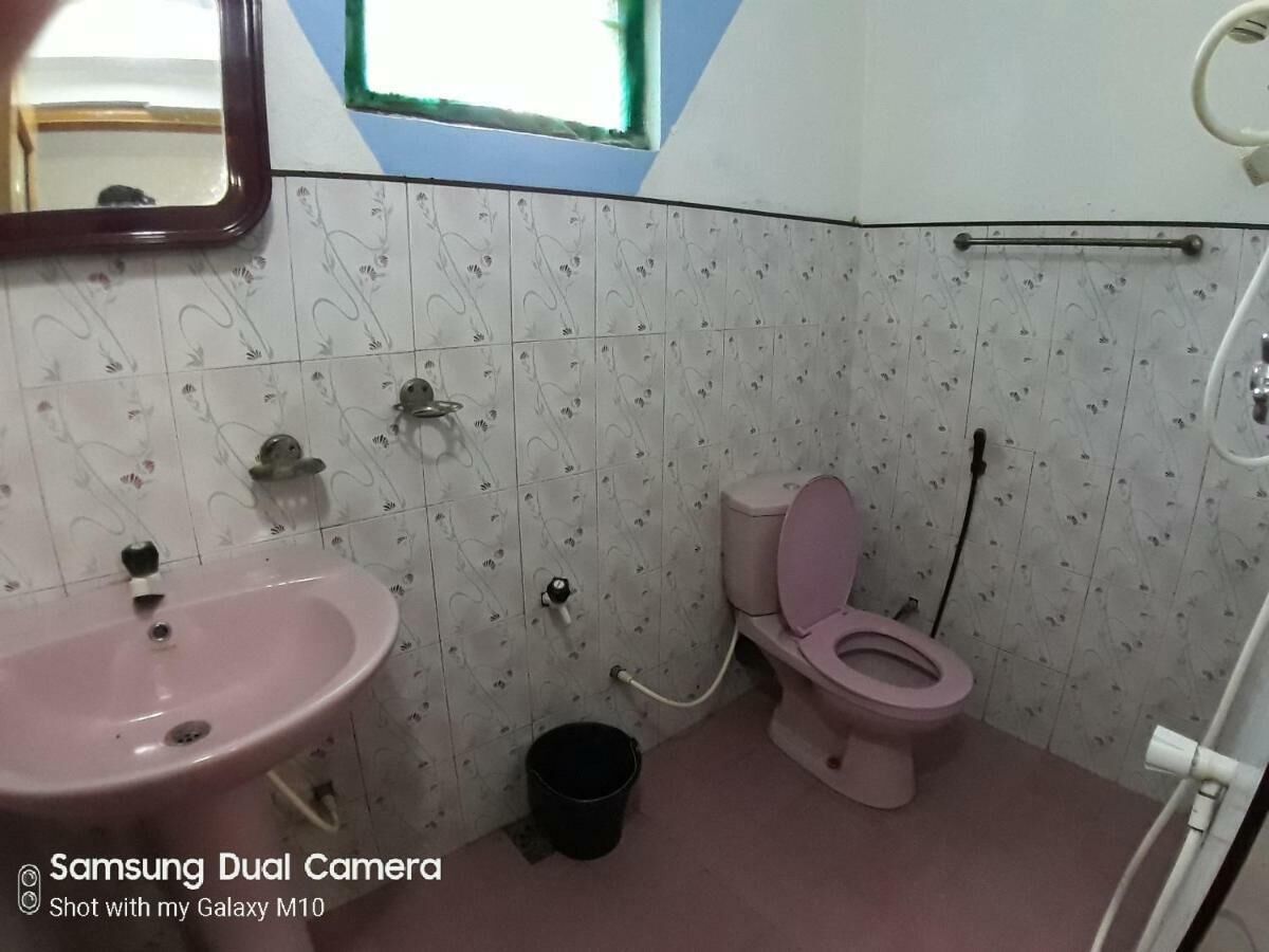 A bathroom with a pink sink, toilet, and a small black bucket.