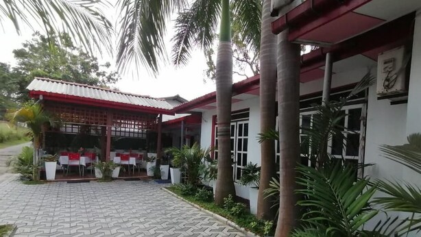 A covered outdoor seating area with tables and chairs, surrounded by palm trees and potted plants. - Dilshan Guest House (Polonnaruwa)