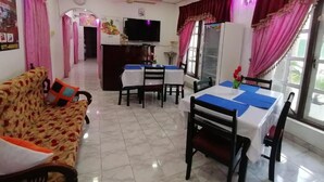 A dining area with tables and chairs, a sofa, a television, and a refrigerator. - Dilshan Guest House (Polonnaruwa)
