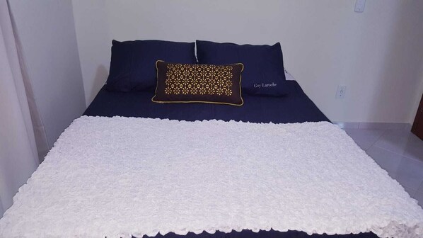 A bed with a white blanket and two navy blue pillows, one with a patterned design.