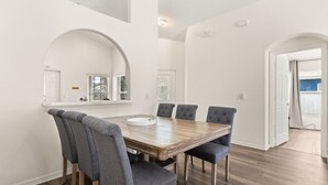 A dining area with a wooden table, grey upholstered chairs, and white walls.