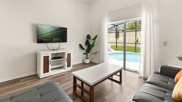 A modern living room with a flat-screen TV, a white cabinet, a dining table, and a gray sofa.