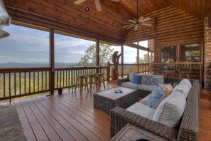 Una terraza de madera con mobiliario de mimbre, un extintor y vistas a las montañas.