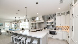 A modern kitchen with a central island, white cabinetry, pendant lights, and a backsplash with a geometric pattern. - Luxury Coastal Estate with Rooftop Deck, Pool and Gulf Views (Bradenton Beach)
