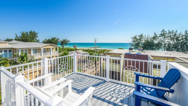 A balcony with a view of the beach, white railings, and blue chairs. - Luxury Coastal Estate with Rooftop Deck, Pool and Gulf Views (Bradenton Beach)