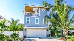 A two-story house with a white garage door, a balcony with a white railing, and a small circular window on the second floor. - Luxury Coastal Estate with Rooftop Deck, Pool and Gulf Views (Bradenton Beach)