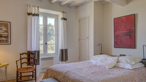 A bedroom with a bed, a chair, a desk, and a window with curtains. - Stone Provencal farmhouse with panoramic view & swimming pool- Saint-Restitut (Saint-Restitut)