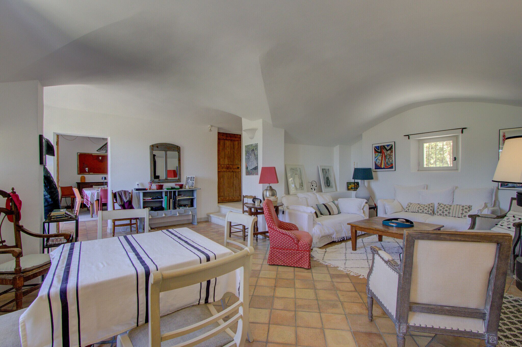 A spacious living area with a dining table, chairs, a sofa, and a red patterned chair.
