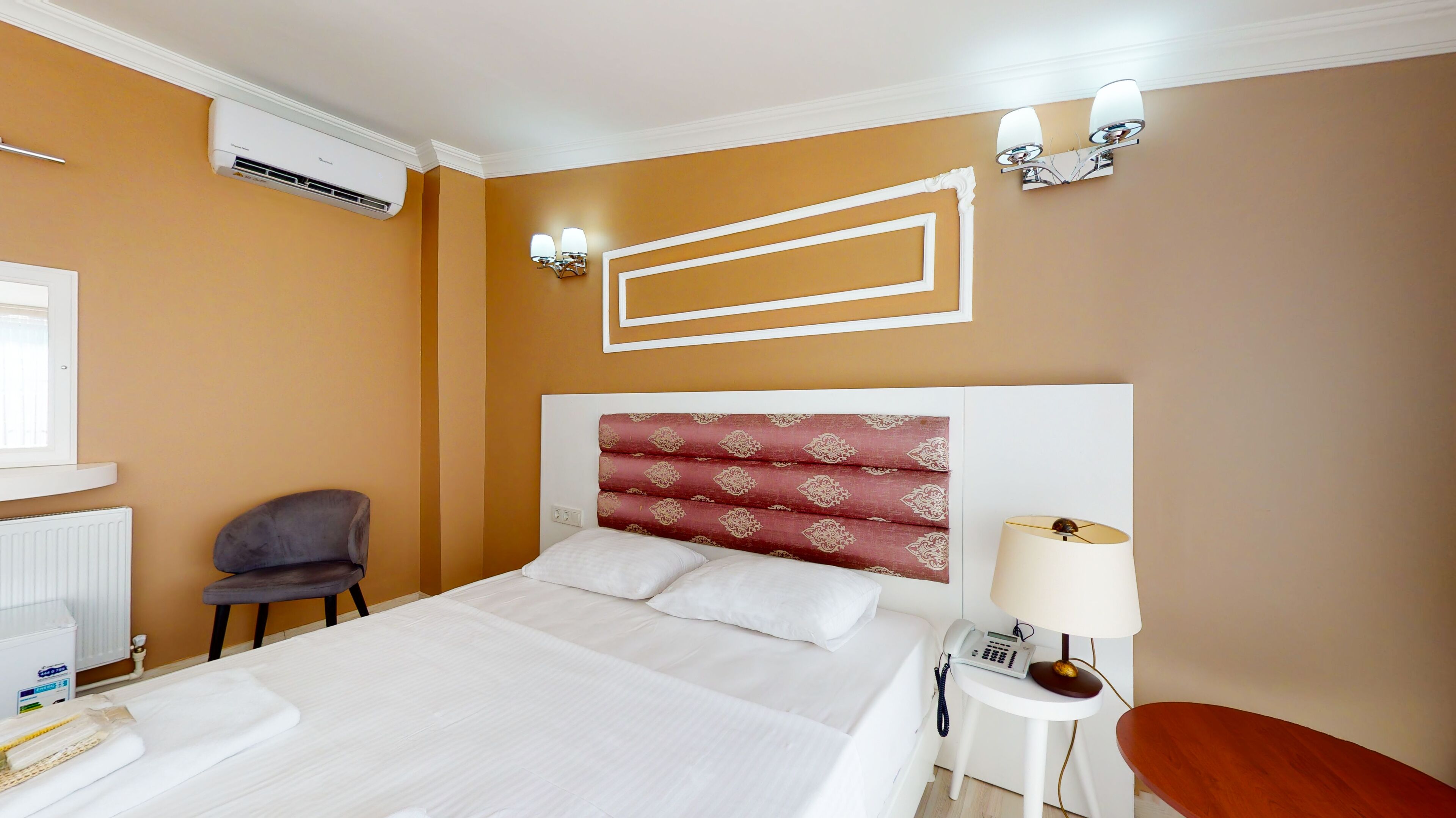 Een hotelkamer met een groot bed, een stoel, een nachtkastje met een lamp, en een wandairconditioner.