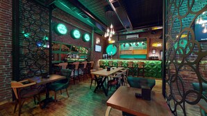 Interior de restaurante con paredes de ladrillo, asientos tapizados en verde, mesas de madera y lámparas colgantes.