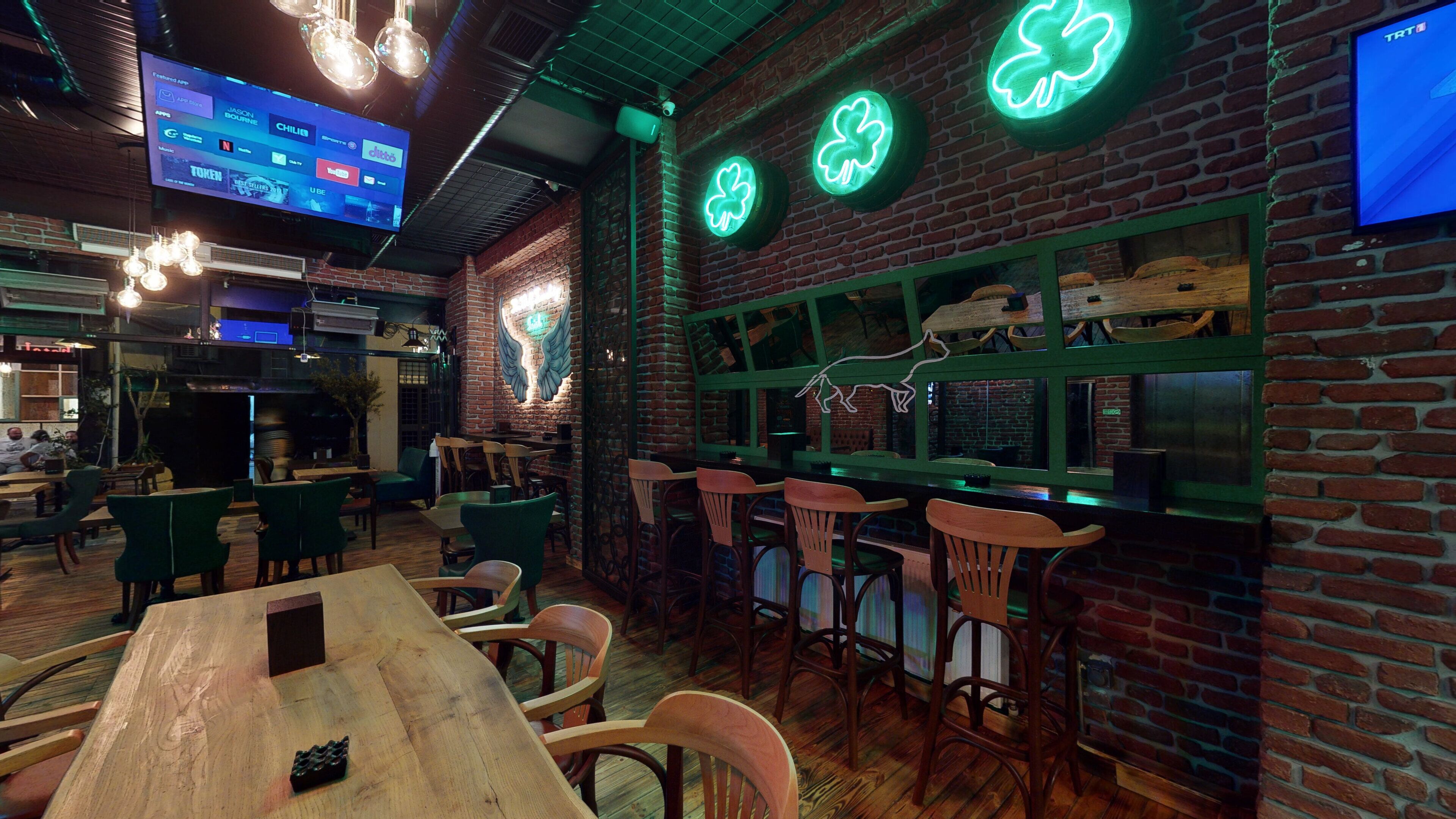 A cozy bar area with brick walls, wooden furniture, and neon shamrock signs.