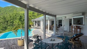 A covered outdoor area with a pool, lounge chairs, and tables.