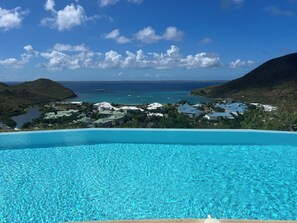 A clear blue infinity pool with a view of a coastal town and the ocean.
