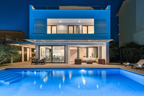 A modern two-story house with a swimming pool in the foreground.