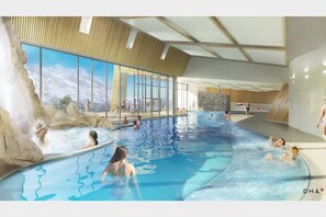 Una piscina interior con vistas despejadas a montañas a través de amplios ventanales, techo de madera y una cascada.