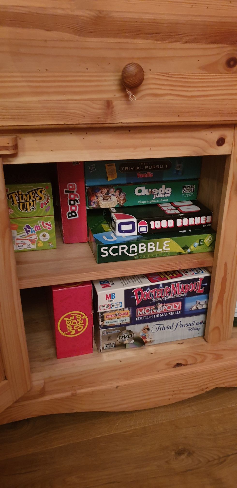 A wooden cabinet with various board games including Scrabble, Monopoly, and Cluedo Junior.