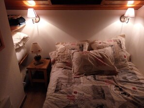Un dormitorio con una cama cubierta con ropa de cama estampada, una mesita de noche con una lámpara y dos lámparas de pared.