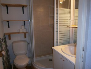 Un baño con inodoro, ducha y lavabo. Hay repisas instaladas en la pared sobre el inodoro.