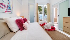 Ein Hotelzimmer mit Bett, Kissen, einem Fernseher und Blick aufs Meer.