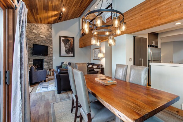 Un comedor con una mesa de madera, sillas, una pared de piedra, chimenea y una cocina moderna al fondo.