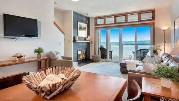 Ein modernes Wohnzimmer mit Kamin, Fernseher und Meerblick.