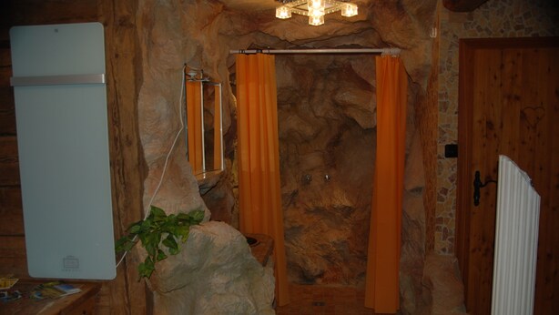 Un baño rústico con pared de piedra, cortina de ducha, lavamanos y radiador blanco.