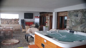 Un jacuzzi en una habitación con paredes de piedra, chimenea, televisor y comedor con sillas y mesa.