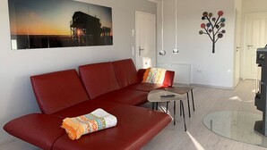 Una sala de estar moderna con un sofá rojo, una mesa de centro de vidrio y un cuadro de un atardecer sobre un muelle.