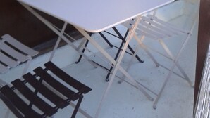 Een gezellig eetgedeelte met een witte tafel en vier stoelen, dichtbij een raam met uitzicht op bomen.