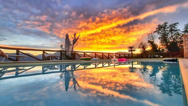 Una piscina amb vistes al capvespre, un pont de fusta i una tanca.