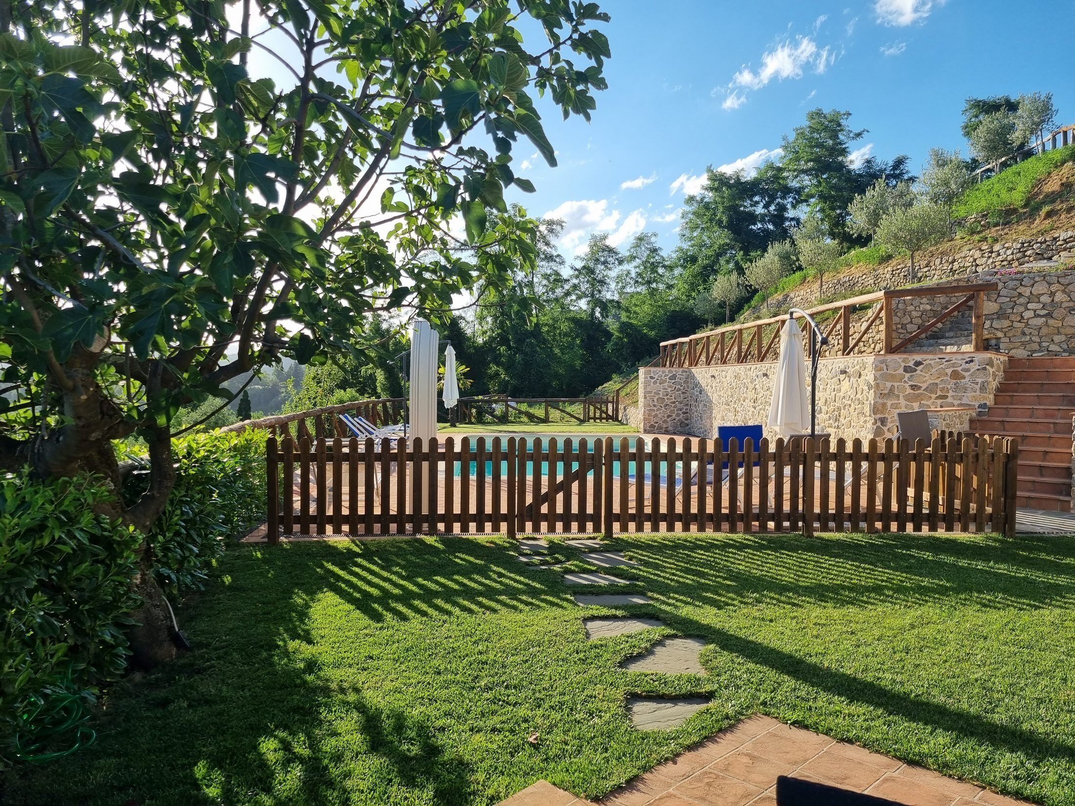Un giardino con piscina, muri in pietra e recinzione in legno.