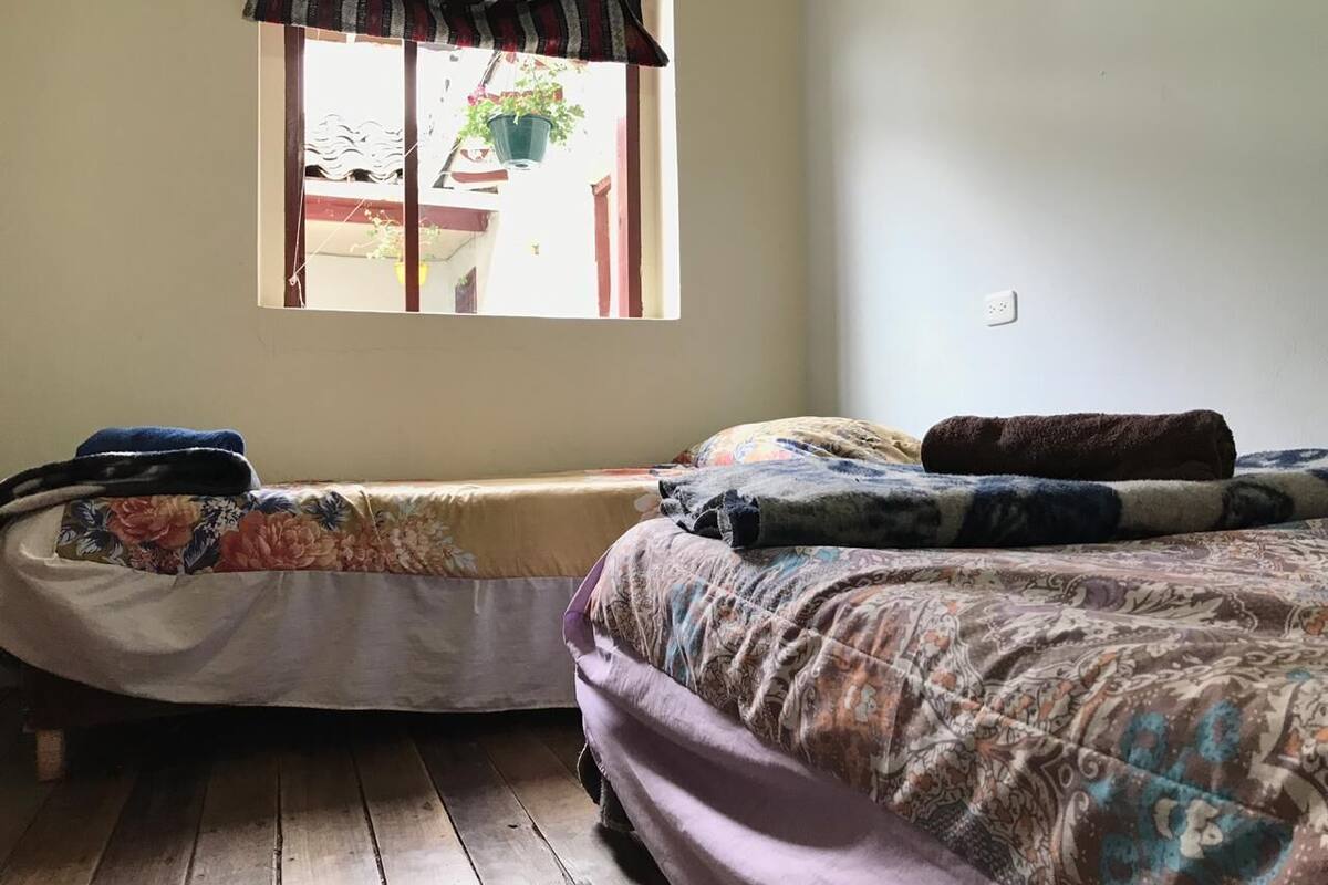 A bedroom with two beds, a window with a curtain, and a wooden floor.
