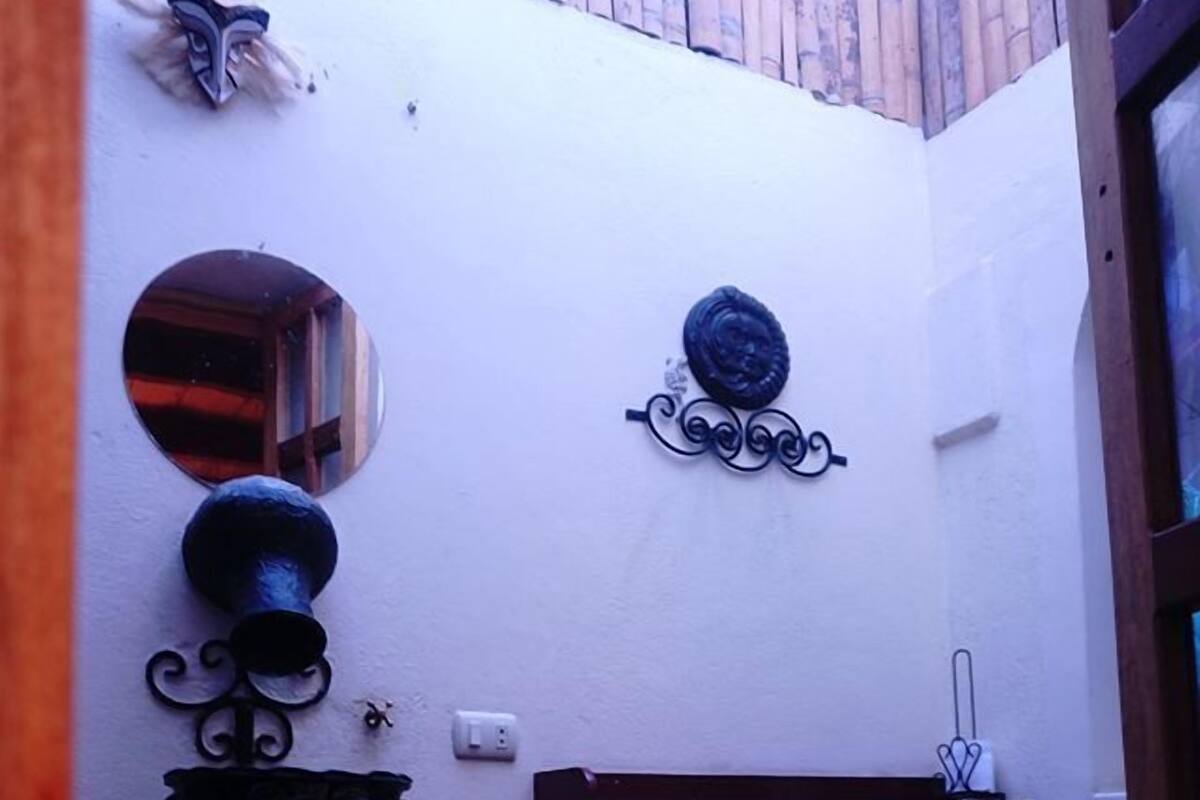 A bathroom with a white wall, a round mirror, a toilet, and a shelf with a hook.