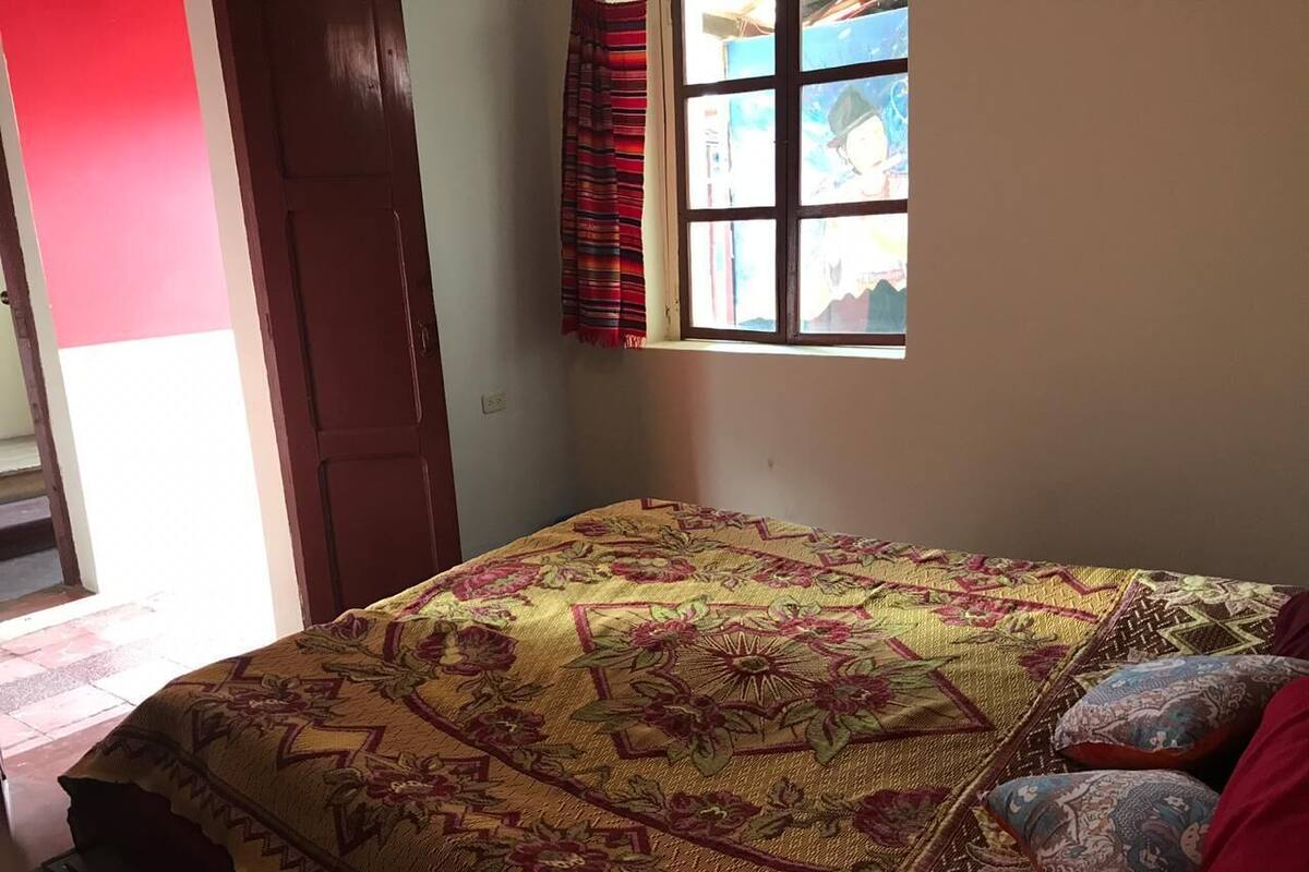 A bed with a patterned bedspread, a window with curtains, and a door in a room.