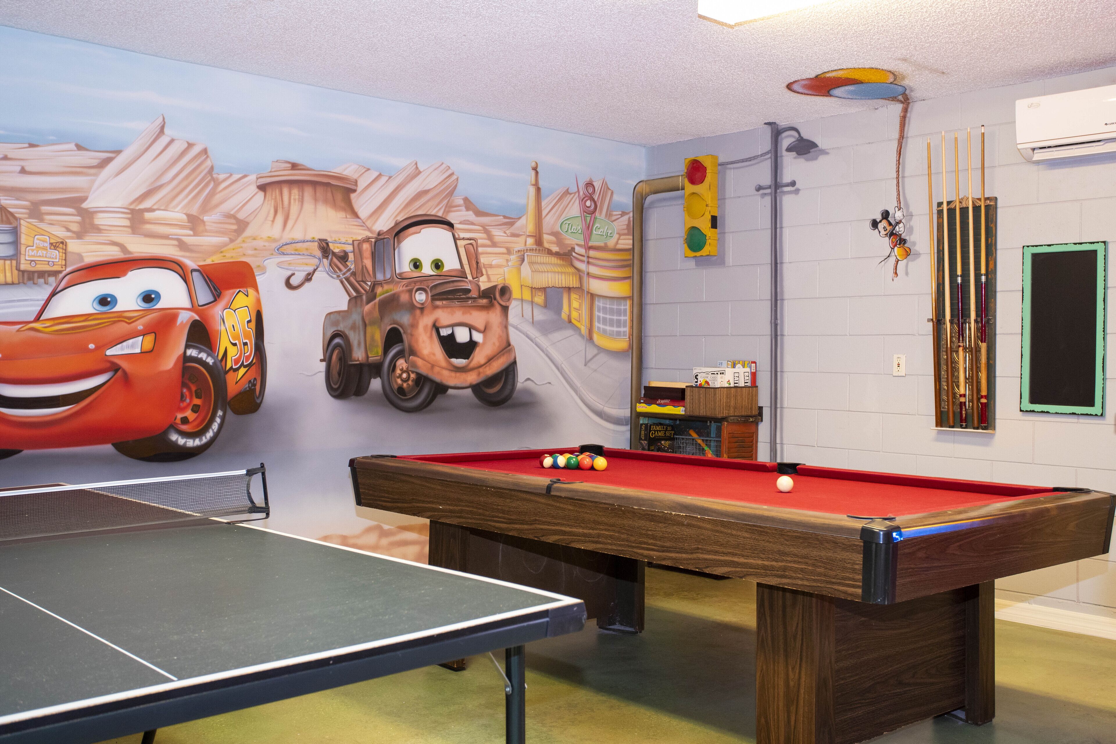 A room with a pool table, a ping pong table, and a mural of animated cars.